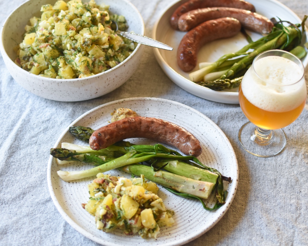 Mayo free potato salad with grilled sausage and veggies. A glass of beer is to the right. 