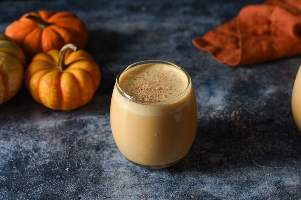 Pumpkin egg nog in front of pumpkins. The egg nog is frothy and layered. 