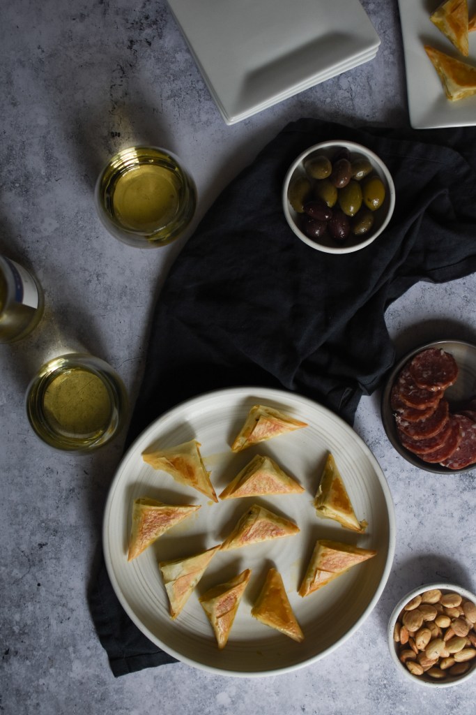 There is a snack spread of kale and fontina phyllo bites, almonds, salami, and white wine. 