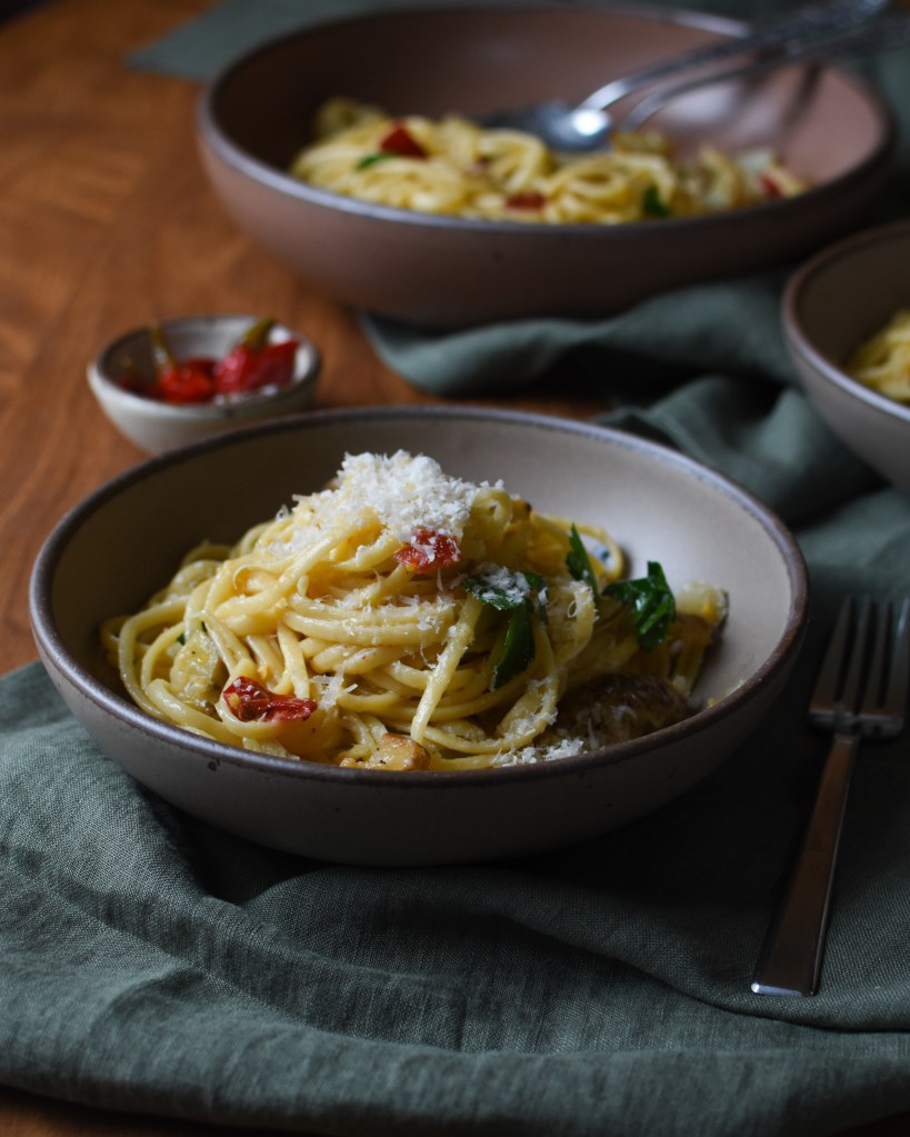 close-up side shot of linguine. You can see a bit of the red Calabrian peppers sticking out, and the sunchokes. It is topped with parmesan. The serving bowl is in the background.